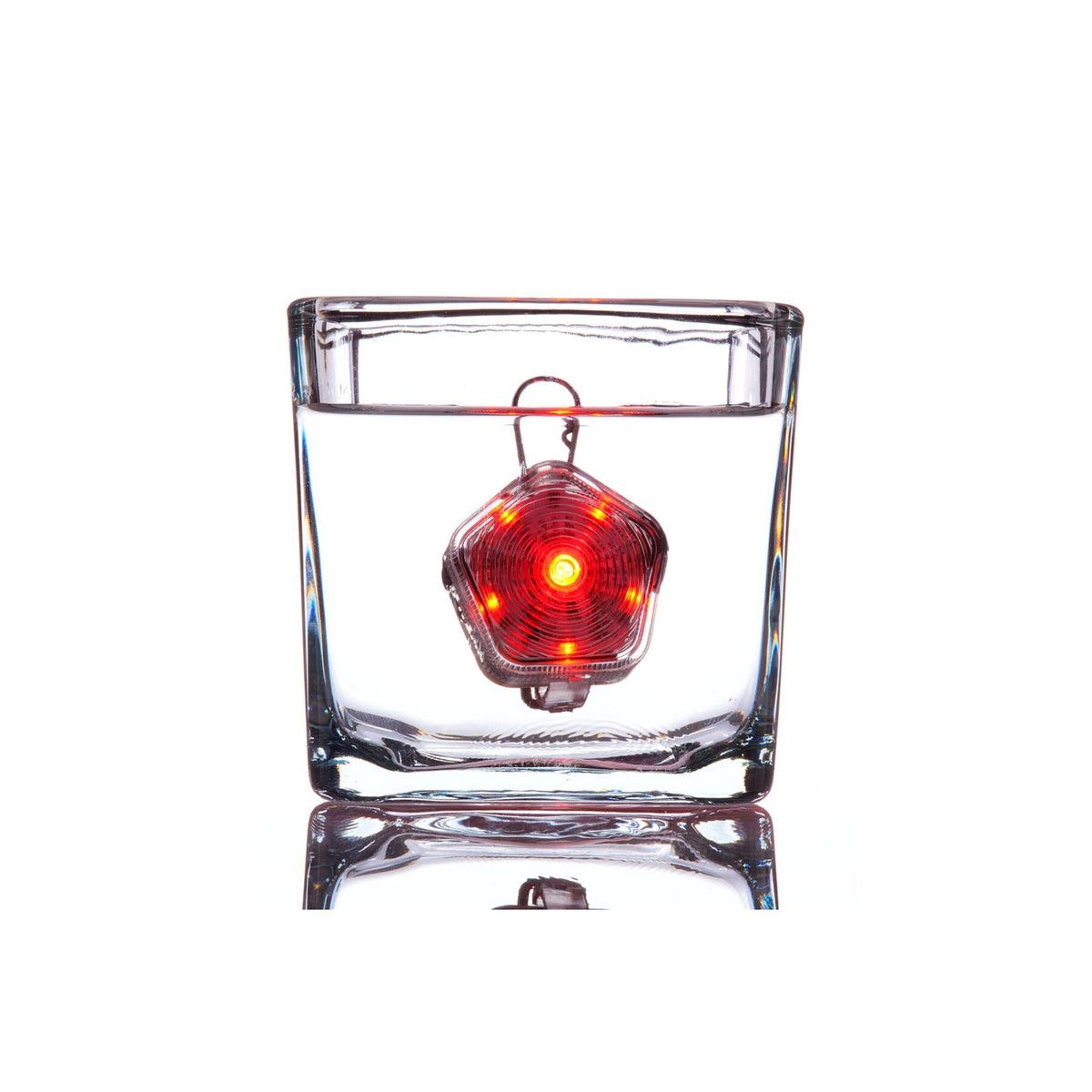 Ruffwear Beacon dog safety light illuminated in red and fully submerged in a glass of water against a white background, demonstrating waterproof performance to 1 metre depth, with the Quick Clip visible above the waterline and the LED glow visible through the water
