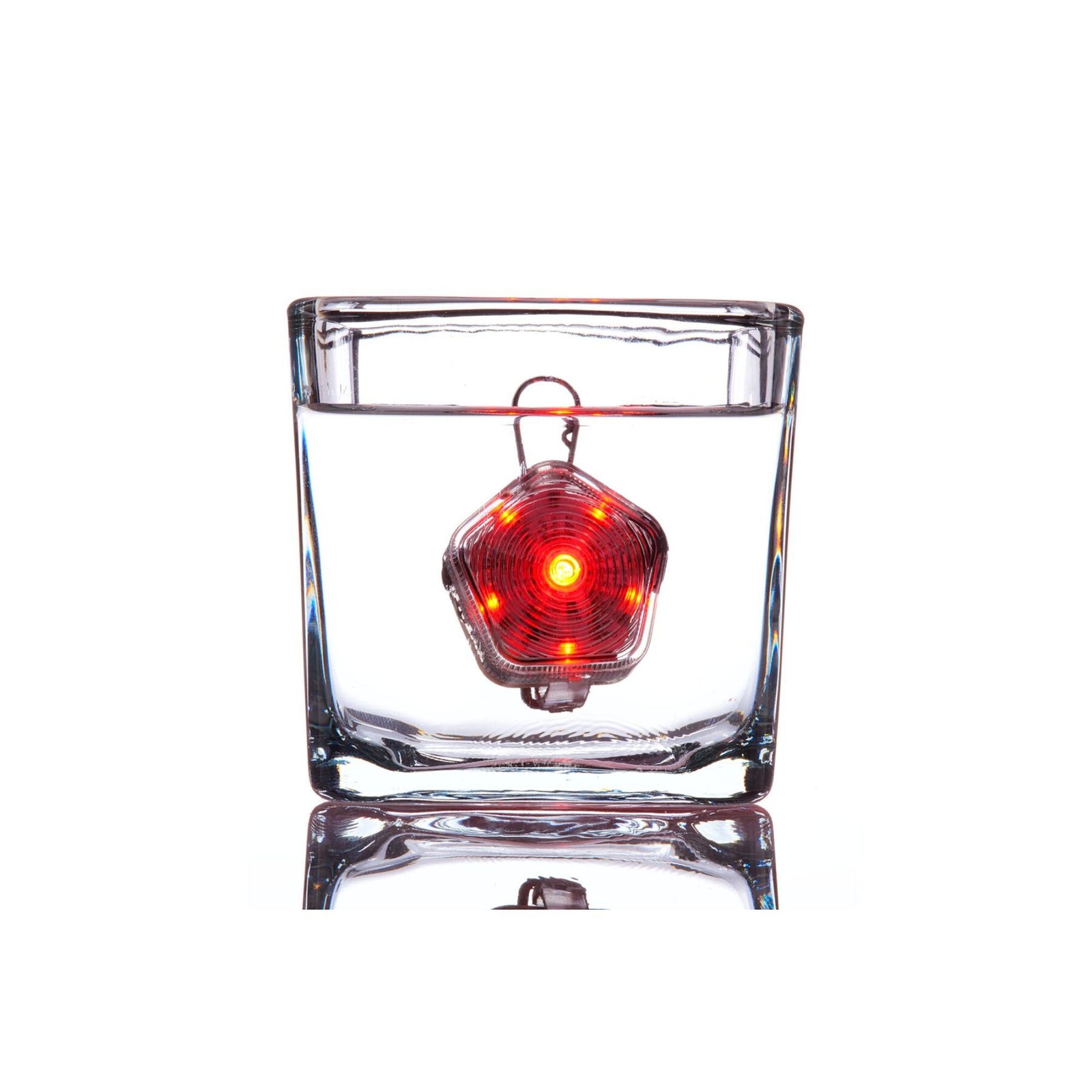 Ruffwear Beacon dog safety light illuminated in red and fully submerged in a glass of water against a white background, demonstrating waterproof performance to 1 metre depth, with the Quick Clip visible above the waterline and the LED glow visible through the water